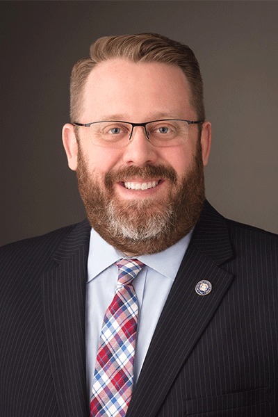 Professional portrait of a bearded man in glasses and a dark pinstripe suit