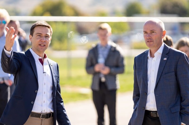 Two men in suits speaking outdoors, one gesturing, at an outdoor event