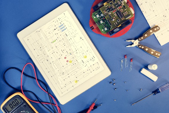 Breadboard circuit prototype with multimeter, pliers, LEDs, and a circuit board on a blue surface