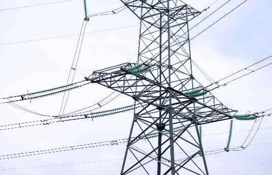 High-voltage electrical transmission tower with power lines against a gray sky