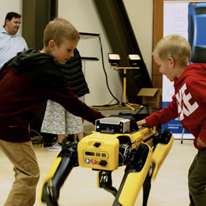 Two children operating a yellow quadruped robot at an ASPIRE open house event