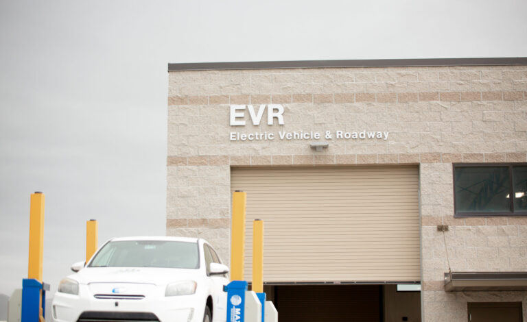 Building exterior with signage reading EVR Electric Vehicle & Roadway and a white electric car parked outside