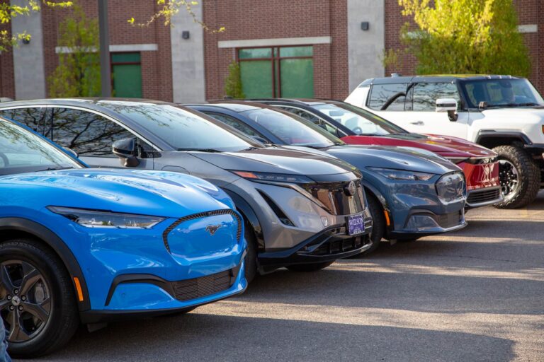 Row of parked electric vehicles including a blue Ford Mustang Mach-E and red GMC Hummer EV