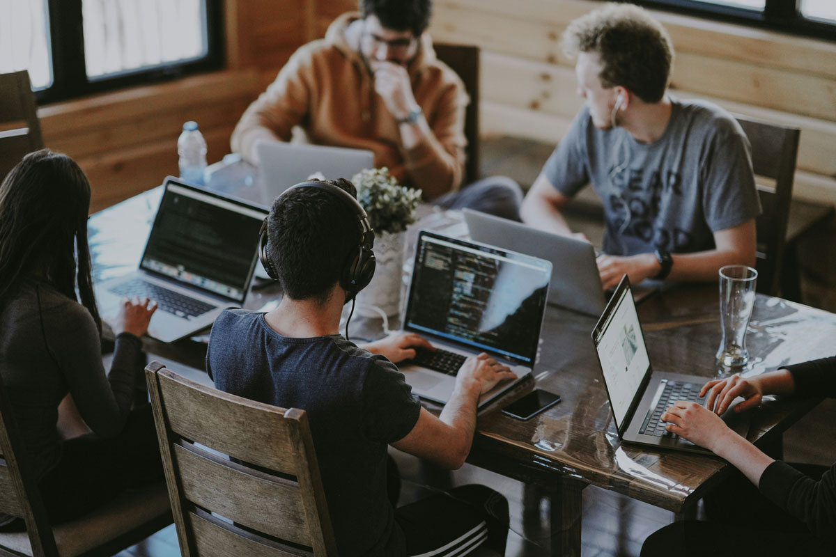 Group of young people working on laptops together around a table in a wood-paneled room