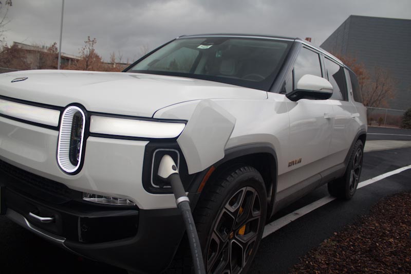 White Rivian R1S electric SUV plugged into a charger on an overcast day