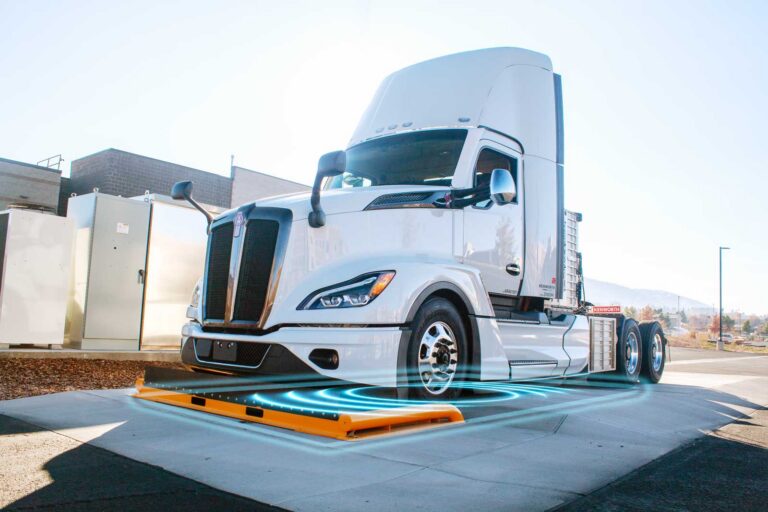 White Kenworth semi truck parked over an orange wireless charging pad emitting blue energy waves