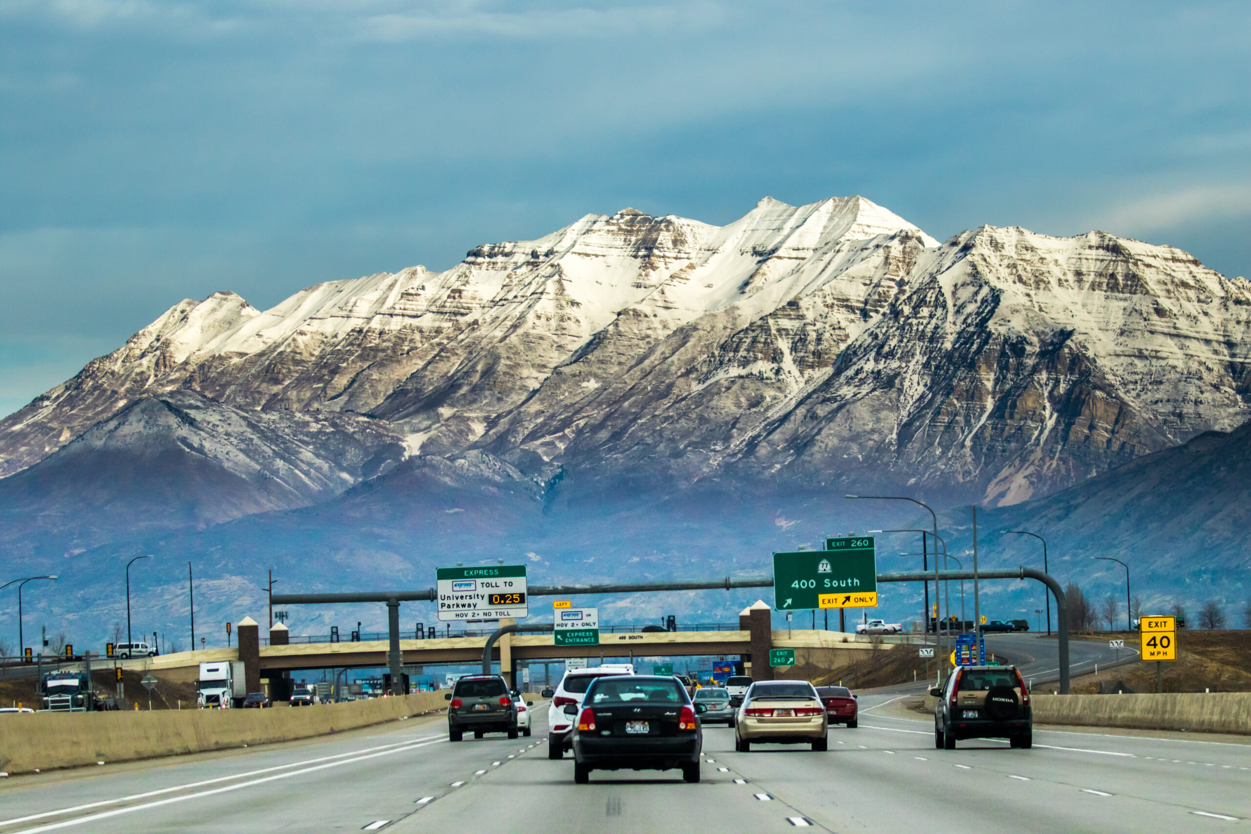 Highway traffic on a multi-lane freeway with snow-capped mountains and exit signs in the background