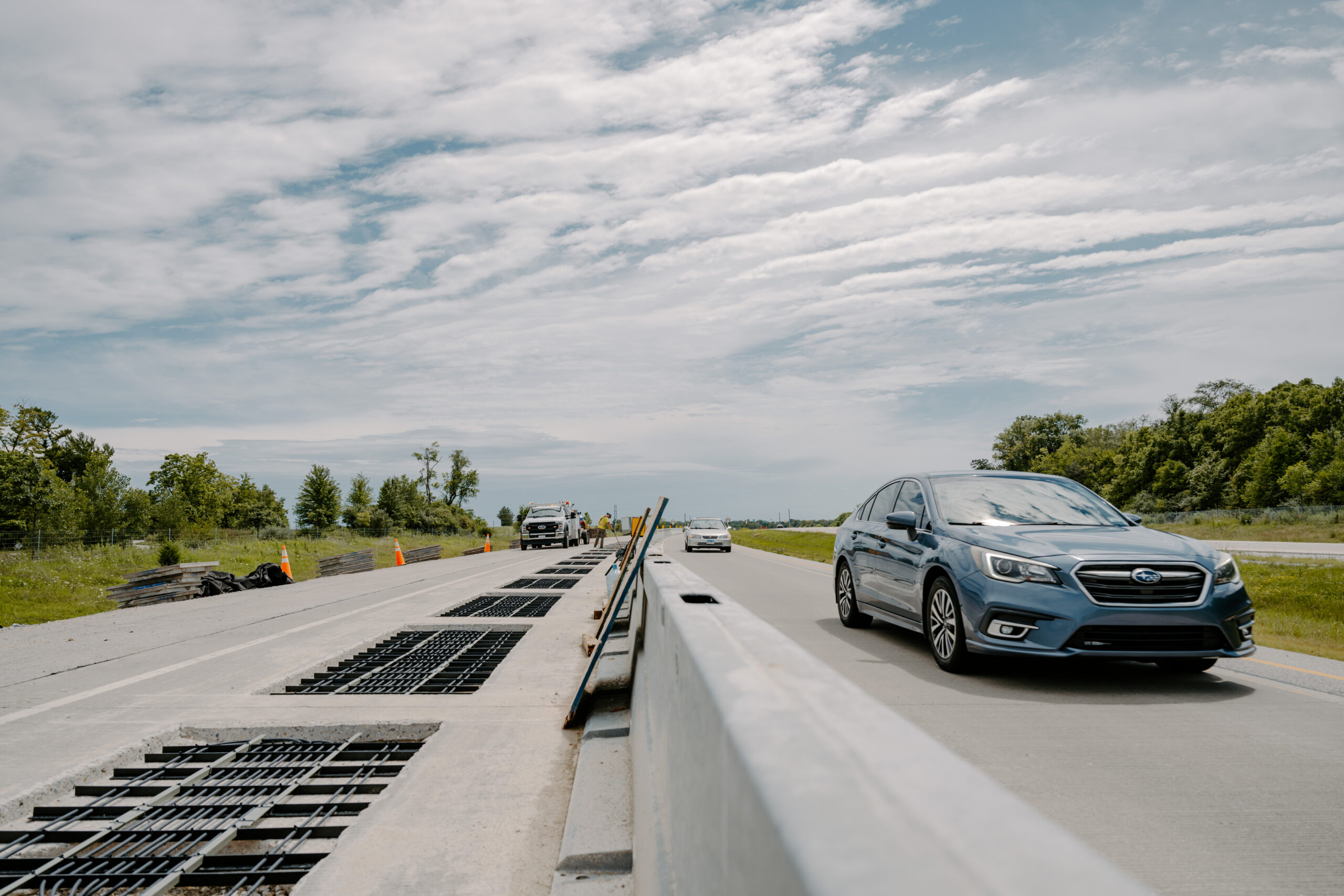 Blue Subaru sedan driving on a roadway beside an electrified pavement construction section