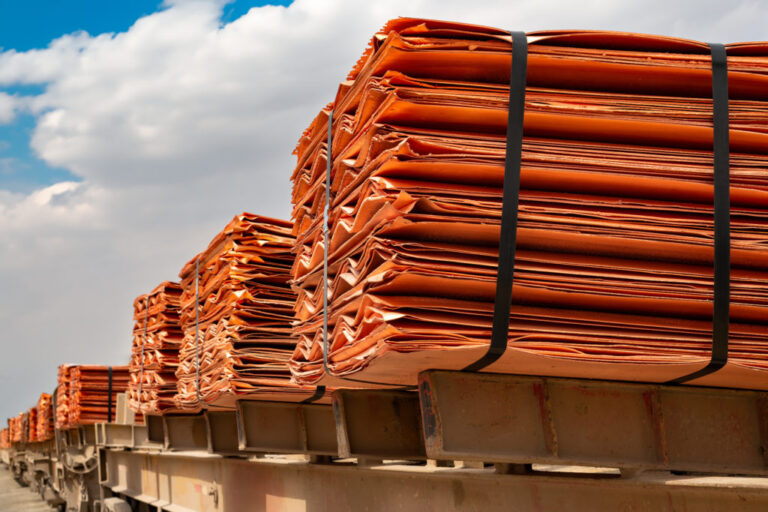 Stacked sheets of refined copper cathodes strapped onto a rail car under a blue sky