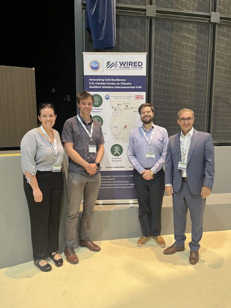 Kyle Goodrick, Masood Parvania, and two others posing in front of the WIRED Grid Resilience Symposium sign.