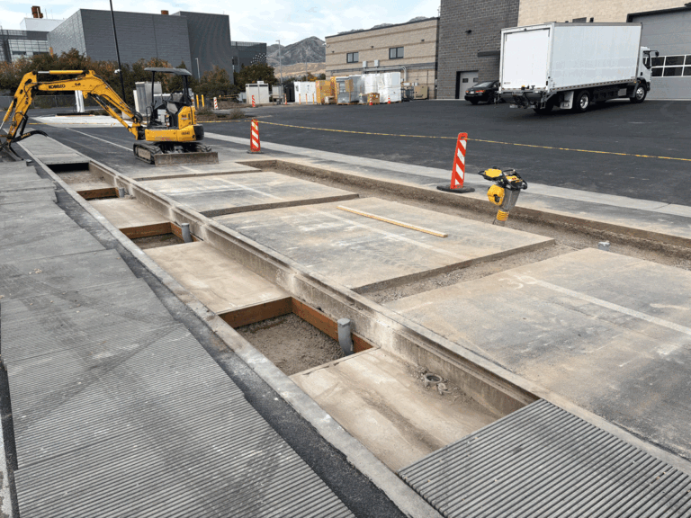 Construction site with mini excavator and exposed concrete trench at a vehicle inductive charging test pad