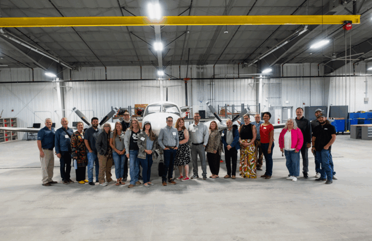 Group of about twenty visitors posing in front of a small aircraft inside an SRDA hangar