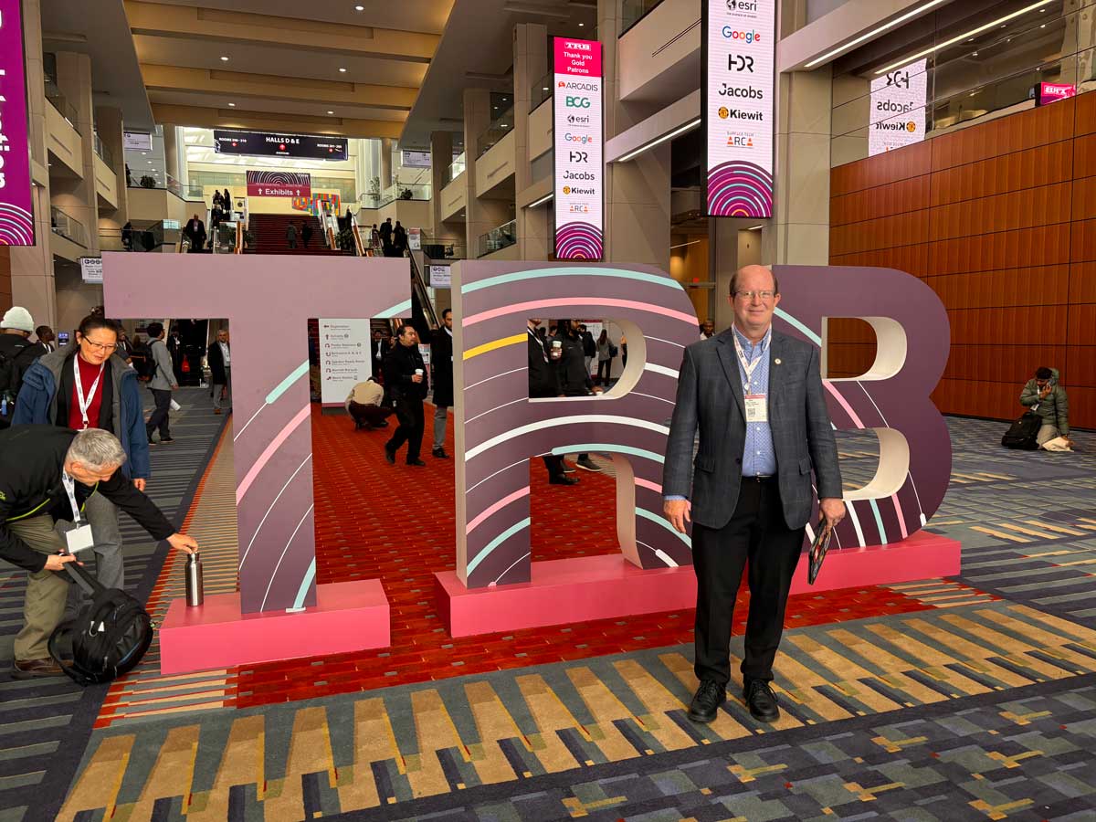 Man in a suit standing in front of large illuminated TRB letter sculpture at the conference
