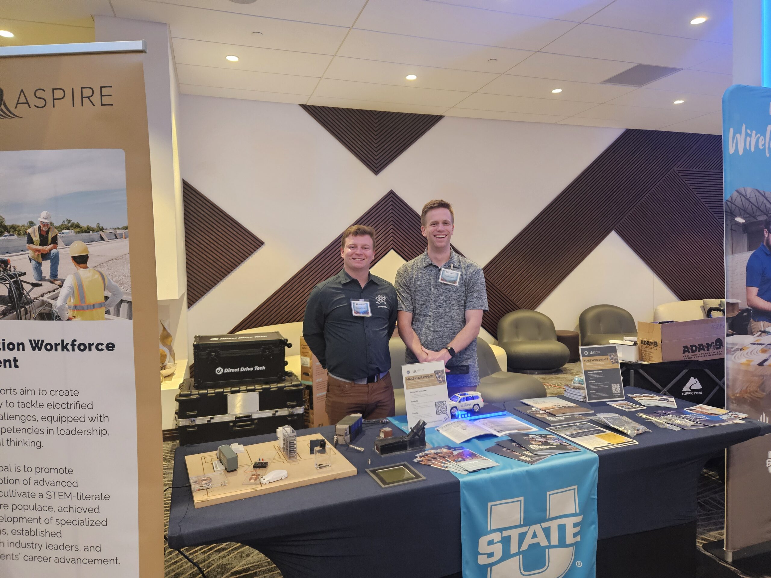 Two men at the ASPIRE and Utah State University exhibit booth with wireless charging displays