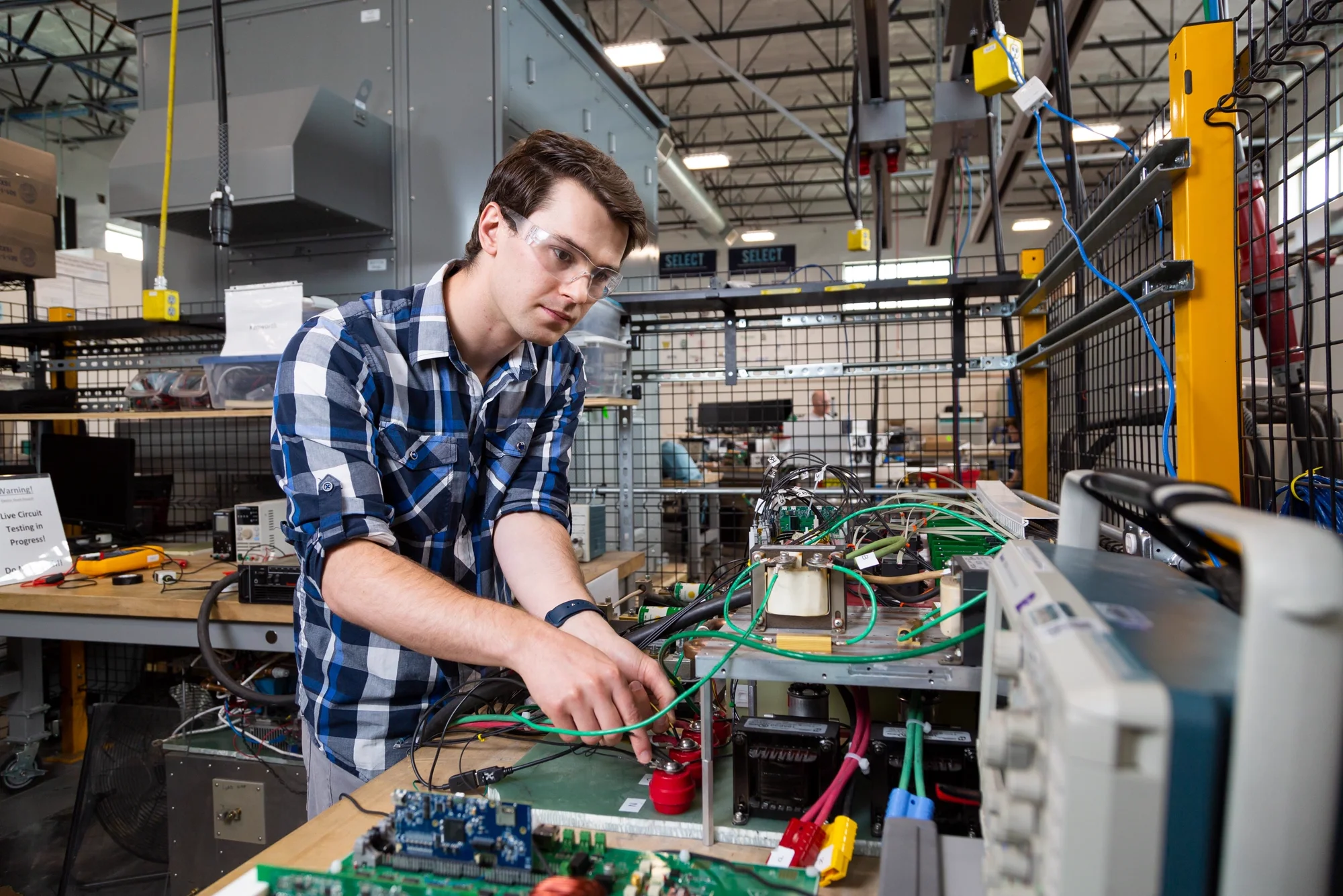 Student in safety glasses working on power electronics and wiring at a lab workbench