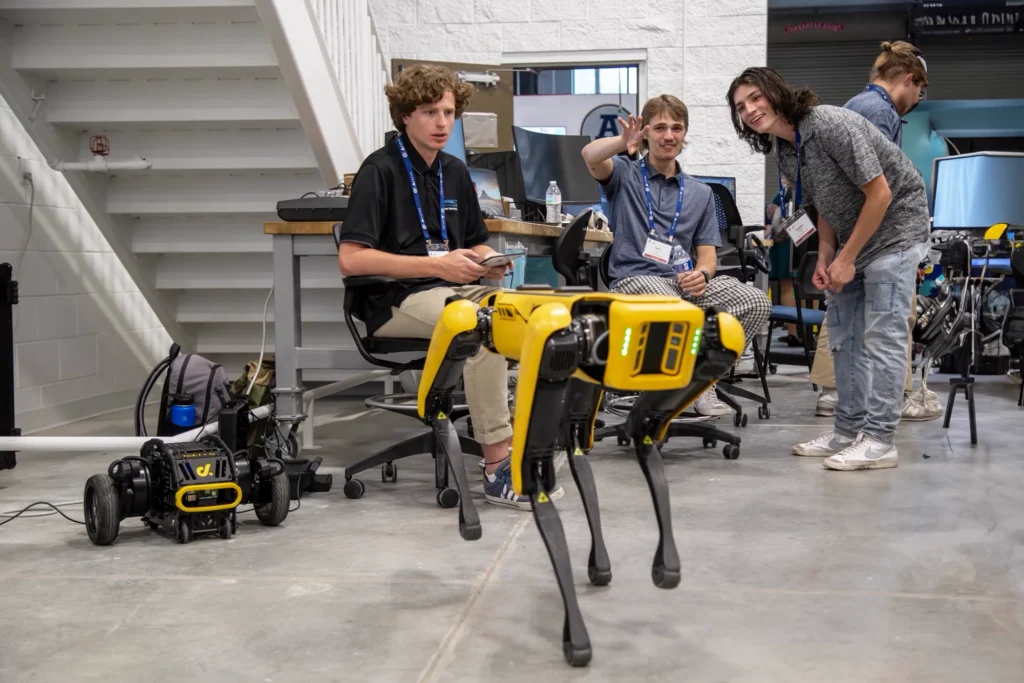 Students watch a yellow Boston Dynamics Spot robot dog demonstration in a lab