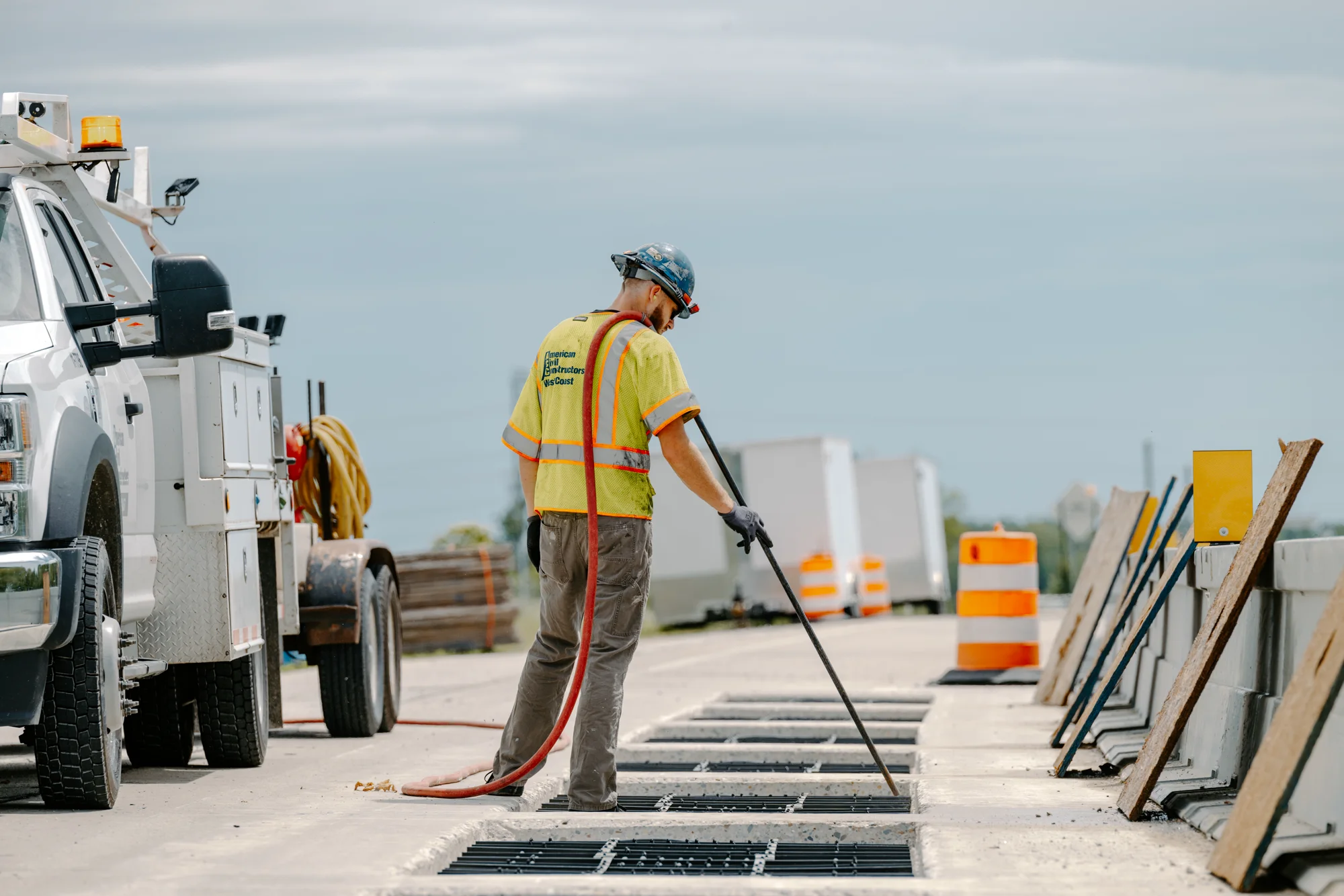 Construction worker in a safety vest installing wireless charging coils in a roadway beside a utility truck