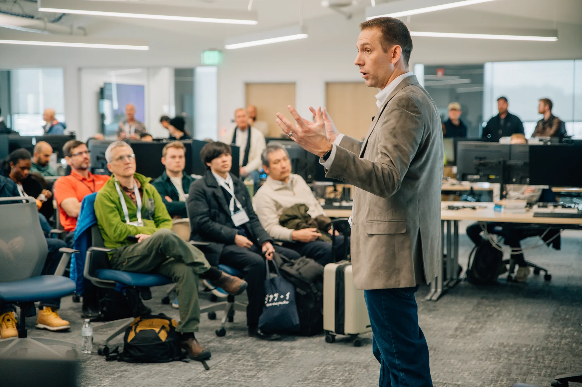 Speaker in a blazer gesturing while presenting to a seated audience at an Innovation Day event