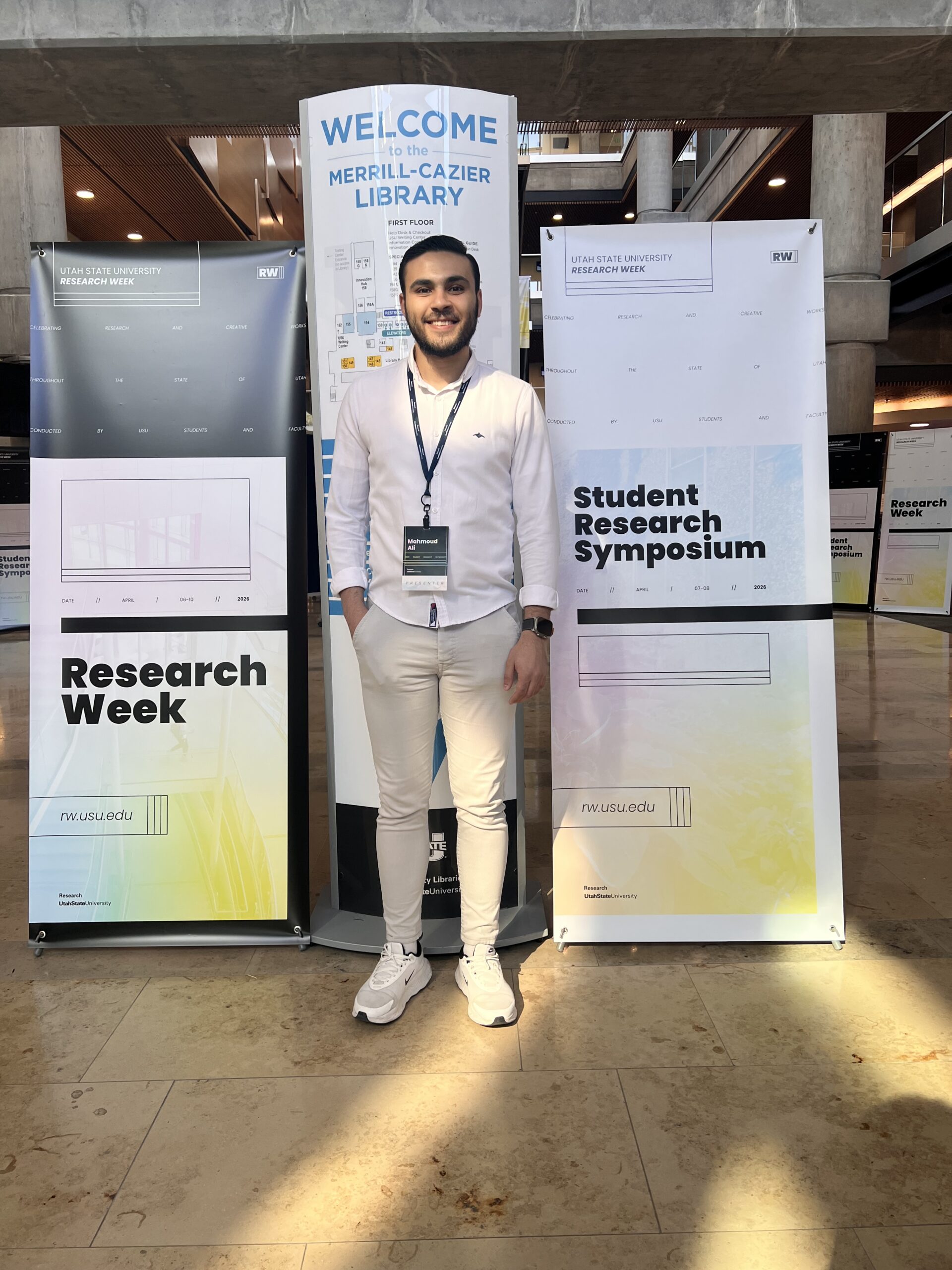 Mahmoud Ali standing between Utah State University Research Week banners at the Student Research Symposium