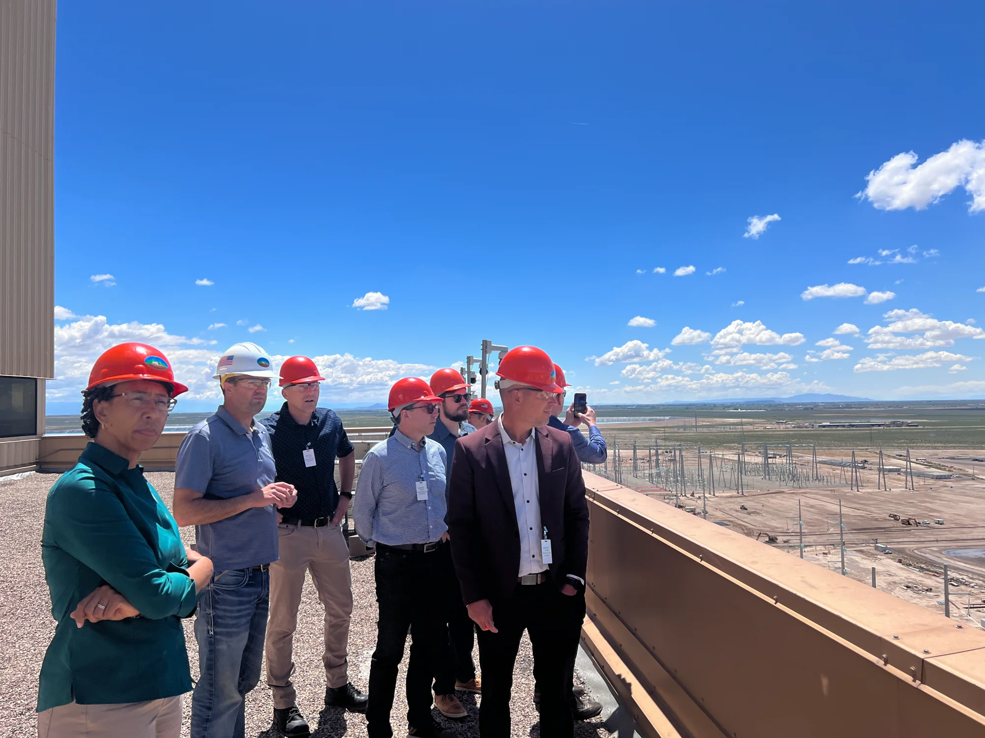 Group wearing red hard hats on an elevated platform overlooking a desert solar facility.