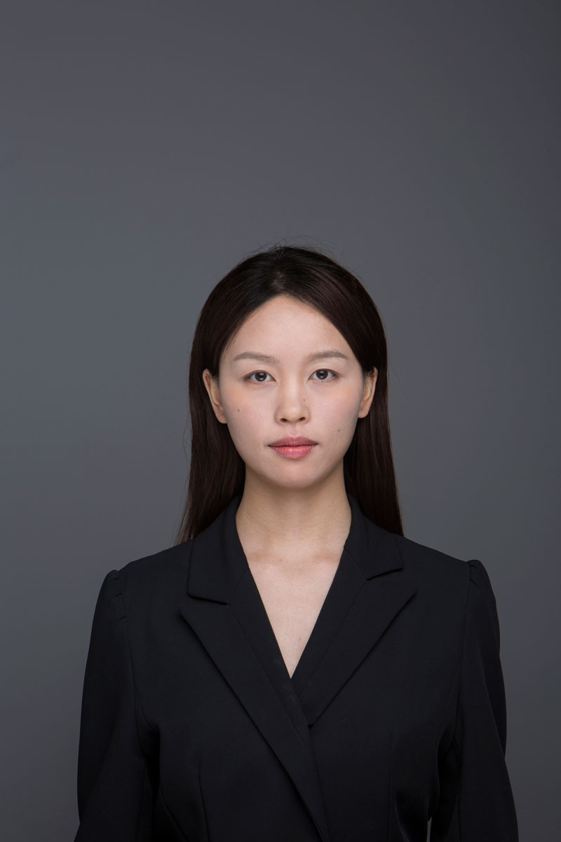 Professional portrait of Qihan in a black blazer against a gray background