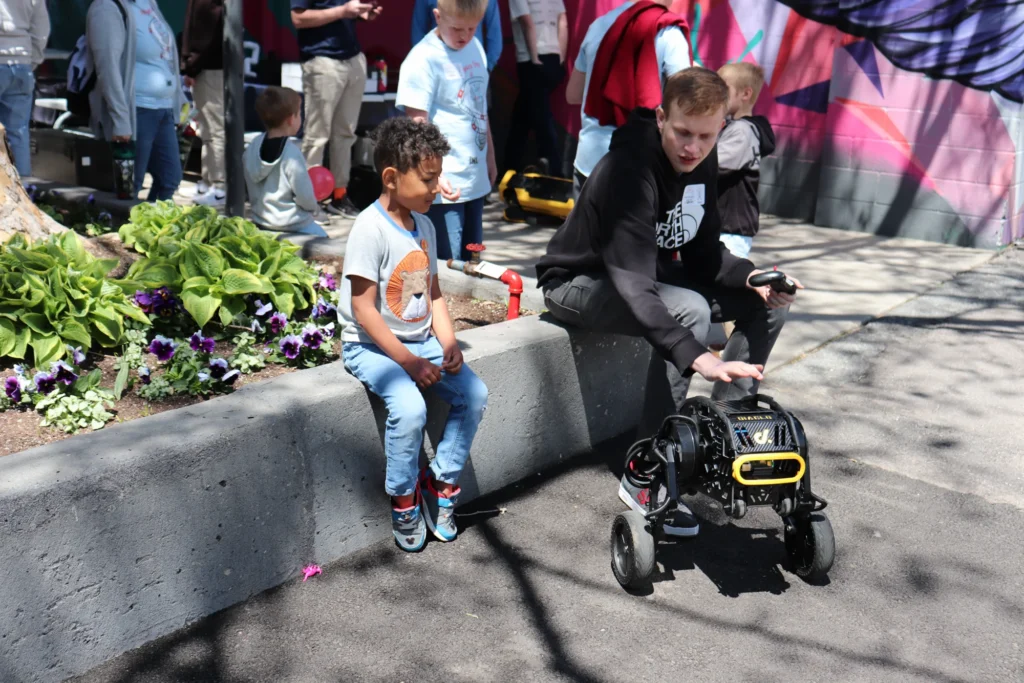 Boy and young man watch a small robot on wheels at USU Physics Day at Lagoon