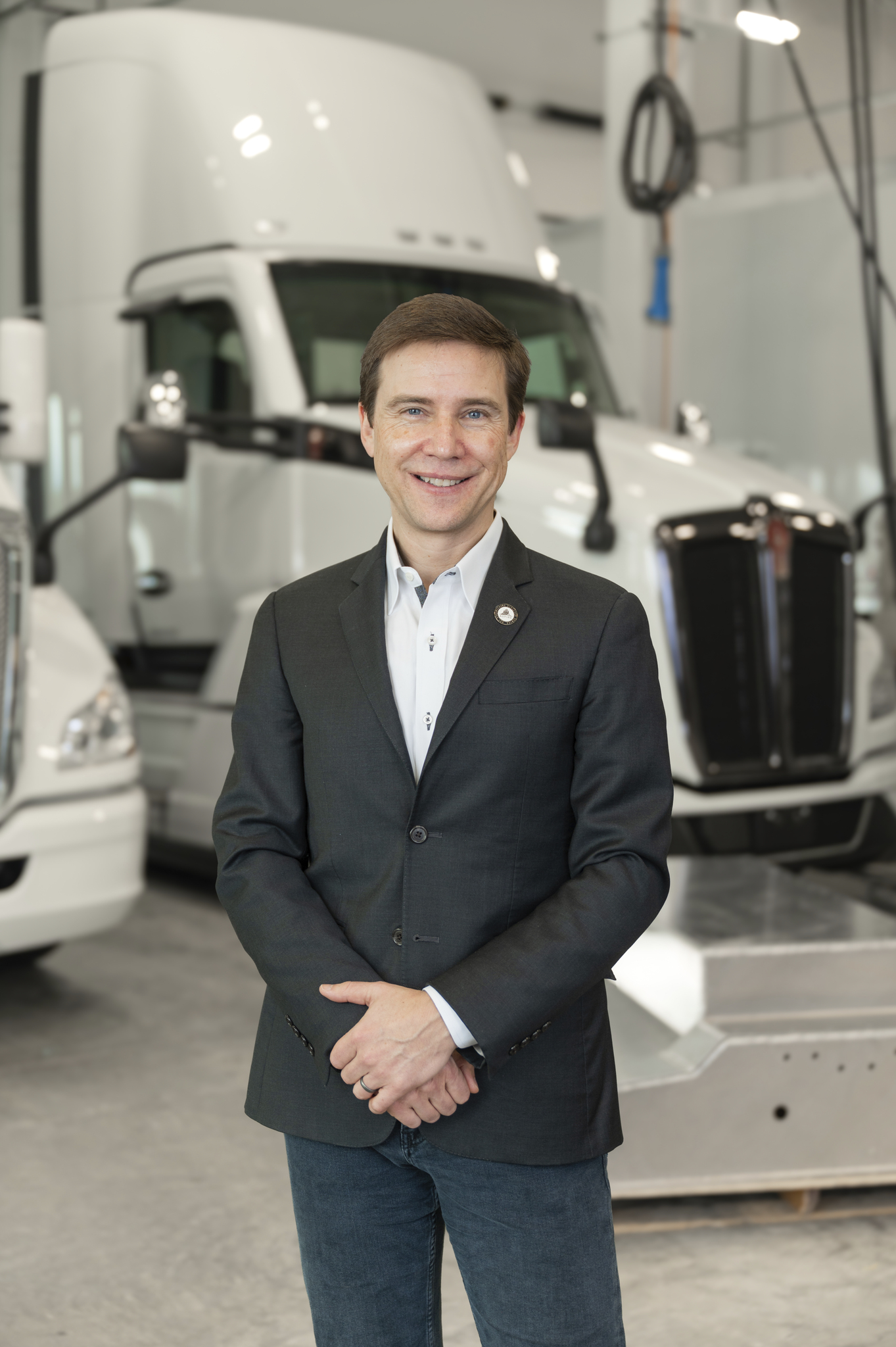 Portrait of Zane in a dark blazer in front of white semi-trucks in a research lab